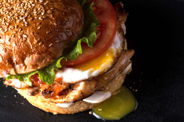rumpled juicy cheeseburger on a black surface, top view, close - up