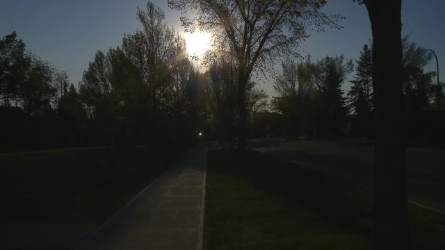 Early morning sun sits above quiet city street. Camera tilts down to include road. White BMW X5 drives by.