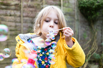 Female child blowing bubbles in the back garden in winter