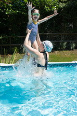 Naklejka premium Female child being lifted into the air, by her mother, in a swimming pool