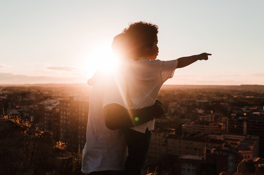 Father and son in a cliff observing the city in a sunset of summer, builds background