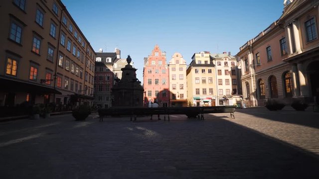 Early morning in the Old Town of Stockholm Sweden, few people around. Man sits on a bench in Stortorget Gamla Stan. Steady glide cam footage moving backwards. Beautiful historical square.