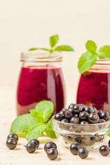 Currant smoothie decorated with fresh green mint leaves and raw ripe berries on yellow pastel background.