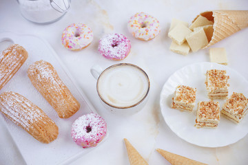 Eclairs and donuts with coffee on a marble background, Light background, Confectionery in a blogger...