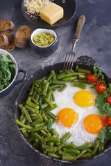 Fried eggs in an old pan with tomatoes, avocado pesto, green beans, pepper and salad on a dark background