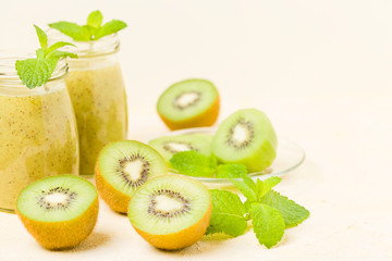 Kiwi smoothie decorated with fresh green mint leaves and raw ripe cut fruit on yellow pastel background.
