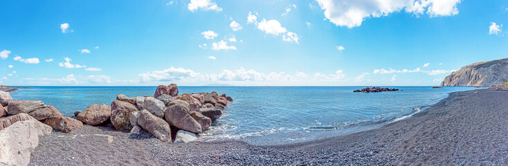 Panorama view of Kamari Beach with breakwater of rocks in the sea, Santorini, Greece