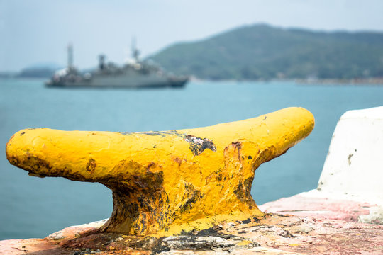 Yellow cleat on naval port with navy ship going to the harbour in the background