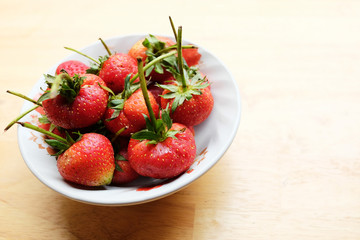 Fresh strawberry in white bowl on wooden table in natural green background.Copy Space