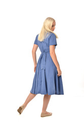 full length portrait of blonde girl wearing blue dress. standing pose with back to the camera. isolated on white  studio background.