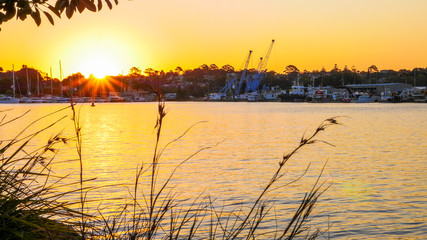 Fototapeta premium Industrial port mix with yacht marina view with sunset sky and flare from the sun.