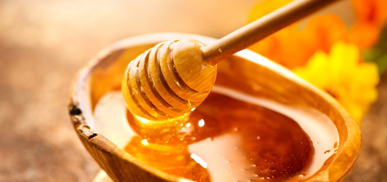 Naklejki Honey. Healthy organic thick honey dripping from the honey dipper in wooden bowl. Sweet dessert background