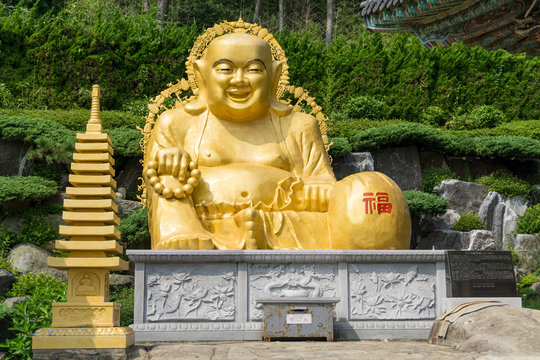 Golden smiling fat Buddha image in sitting position statue at Haedong Yonggungsa Temple in Busan, South Korea.