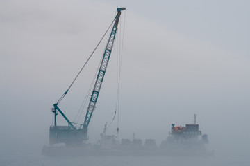 Crane barge in the middle of heavy mist blow from the sea.