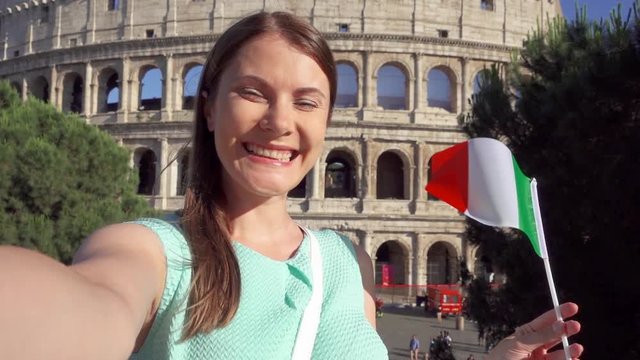 Woman doing selfie near famous attraction Colosseum in Rome, Italy. Teenage girl waving Italian flag in slow motion. Happy female tourist enjoying her european vacation. Student travel through Europe