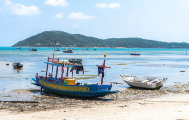 Naklejka na ściany i meble Small wooden and fiberglass fishing boats mooring at the dirty beach in front of fisherman village in Thailand on the sunny day with big island in the background