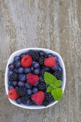 mix of blueberries, blackberries, raspberries in white bowl on old wooden table background