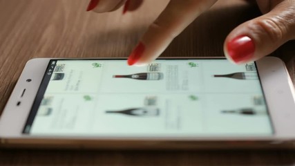 Woman orders red wine home in an online store. Female selects the alcohol in the grocery online store. Close-up. 4K UHD. Screen is blurred.