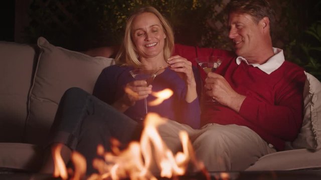 Couple enjoying fire pit at night on terrace enjoying cocktail