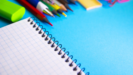 School supplies on blue background. Pens, pencils, ruler, paper clips, notebook for copyspace and marker on the table. View from above with copy space