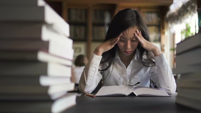 Tired female asian sudent lawyer in white shirt trying to concentrate reading books in the library. Portrait. Indoors.