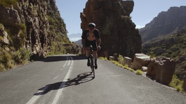 Tracking shot of a fit cyclist doing uphill bicycle ride. Man climbing up the mountain road on a bicycle. 