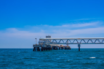 Fototapeta na wymiar Oil fuel pipeline tube on jetty to the sea and blue sky background