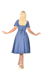 full length portrait of blonde girl wearing blue dress. standing pose with back to the camera. isolated on white  studio background.