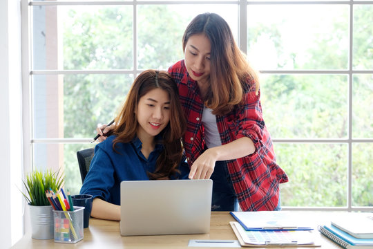  Two young asian women working with laptop computer at home office with happy emotion, working from home, small business, office casual lifestyle concept