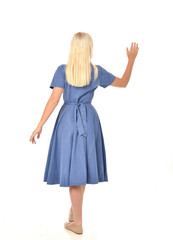 full length portrait of blonde girl wearing blue dress. standing pose with back to the camera. isolated on white  studio background.