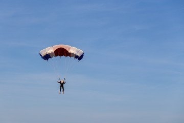 isolated skydiver in colorful parachute gliding after free fall jump with blue sky background