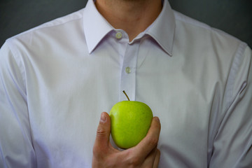 Junger Mann in weißem Hemd hält einen grünen Apfel vor sich