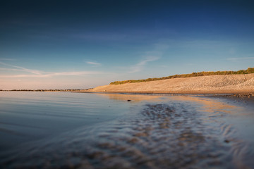 Evening seascape beach scene with waves and blue sky and yellow sand dunes