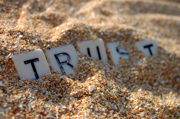Letters of word 'trust' being buried in sand