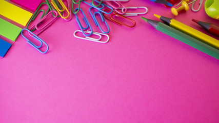 Stationery on pink background. Pens, pencils, scissors, paper clips, color push pins and on the table. View from above with copy space