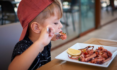Little boy eating tasty octopus
