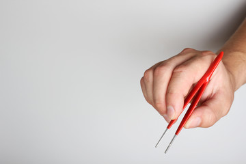 red tweezers in hand on a light background