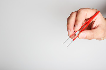 red tweezers in hand on a light background