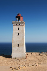 Fototapeta na wymiar Bright beach sand dunes with the famous danish landmark lighthouse with blue sky background. Rubjerg Knude Lighthouse, Lønstrup in North Jutland in Denmark, Skagerrak, North Sea