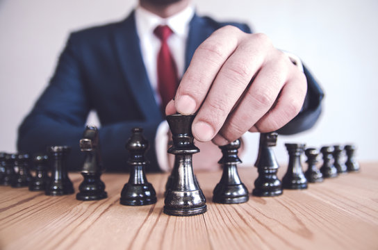 Retro style image of a businessman with clasped hands planning strategy with chess figures on an old wooden table.