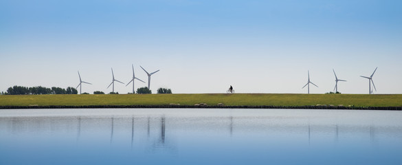 Cyclist drives on the dike. Nearby are wind turbines
