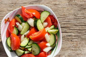Fresh vegetable salad  with tomatoes, cucumbers, onion and olive oil on wooden table. Top view
