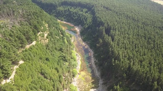 Aerial drone view descending towards a lake located inside a narrow, tree lined, steep sided canyon