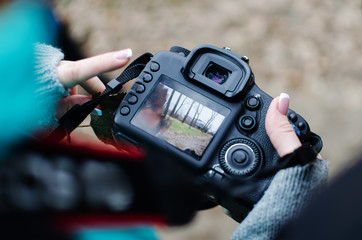 girl is looking at the frame on the camera screen. A girl photographer with a French manicure in a park in the fall.