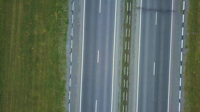 Aerial view of several parallel roads in the middle of the park zone in summer. Cinematic drone shot flying over road with traffic in green fields