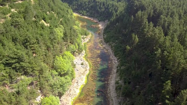Aerial drone view descending into a narrow tree lined canyon containing a small lake at the bottom