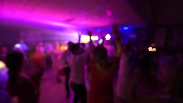 Disco party all night long with defocused view of great wedding party with silhouettes of people dancing on the dancefloor with blue disco lights glowing in the background multiple colors
