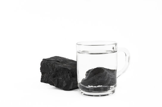 Water purification with black Shungite stones, clear drinking glass with stones on gray background. Removing toxins and organic matter from the water, isolated on white.