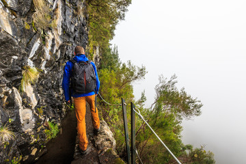 Man walking a levada trail with Steep abyss next to the trail in the mountains of Madeira, Portugal