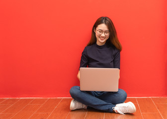 Happy young woman sitting on the floor with crossed legs and using laptop on gray background